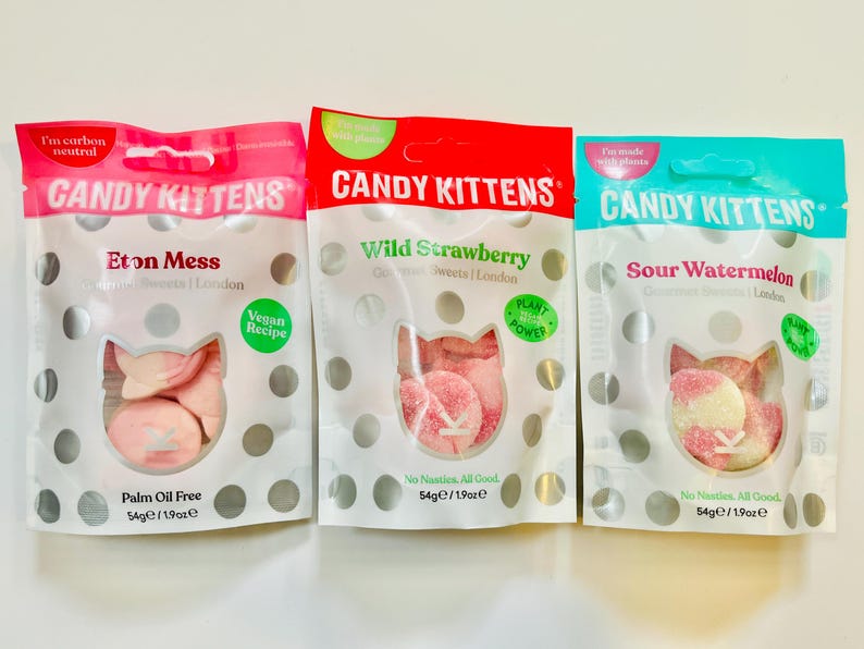 May include: Three individually packaged bags of vegan candy kittens. The bags are pink, red, and blue. The flavors are Eton Mess, Wild Strawberry, and Sour Watermelon. Each bag has a white polka dot pattern and a picture of pink candy kittens.