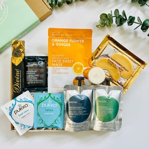 May include: A gift box filled with self-care items, including face masks, eye masks, tea bags, and bath products. The box is decorated with green and white paper and includes the text "Happiness in a Box".