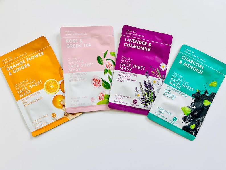 May include: Four different face sheet masks with various scents and ingredients. The masks are pink, purple, teal, and yellow. The scents are Rose & Green Tea, Lavender & Chamomile, Charcoal & Menthol, and Orange Flower & Ginger.