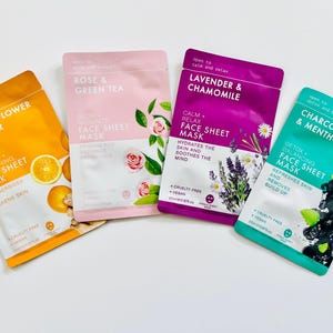 May include: Four different face sheet masks with various scents and ingredients. The masks are pink, purple, teal, and yellow. The scents are Rose & Green Tea, Lavender & Chamomile, Charcoal & Menthol, and Orange Flower & Ginger.
