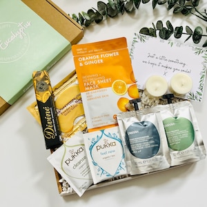 May include: A gift box filled with self-care items, including face masks, bath products, and chocolate. The box is decorated with a green and white label that says "White Eucalyptus". The card says "Just a little something we hope it makes you smile!"