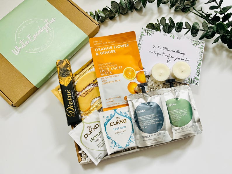 May include: A gift box filled with self-care items, including face masks, bath products, and chocolate. The box is decorated with a green and white label that says "White Eucalyptus". The card says "Just a little something we hope it makes you smile!"