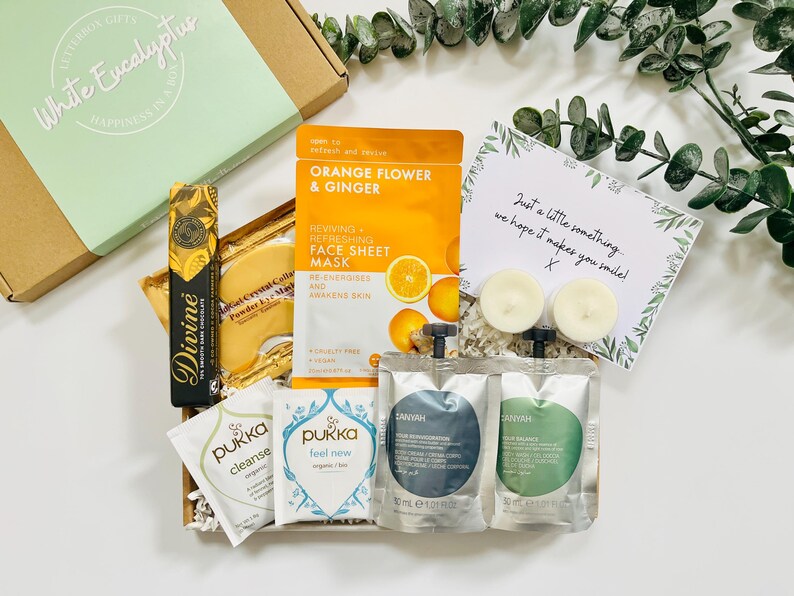 May include: A gift box filled with self-care items, including face masks, bath products, and candles. The box is decorated with white tissue paper and a handwritten note that says "Just a little something, we hope it makes you smile!"