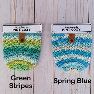 K&ouml;nnte beinhalten: Zwei geh&auml;kelte Pint-Becherw&auml;rmer. Einer ist gr&uuml;n-blau gestreift und der andere blau-wei&szlig; gestreift. Beide haben ein braunes Leder-Etikett mit der Aufschrift "handmade pint cozy".