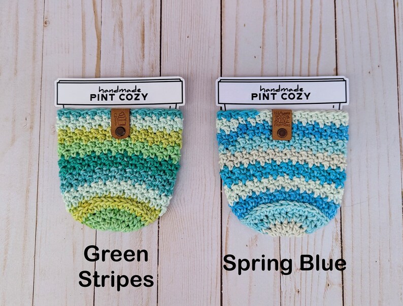 K&ouml;nnte beinhalten: Zwei geh&auml;kelte Pint-Becherw&auml;rmer. Einer ist gr&uuml;n-blau gestreift und der andere blau-wei&szlig; gestreift. Beide haben ein braunes Leder-Etikett mit der Aufschrift "handmade pint cozy".