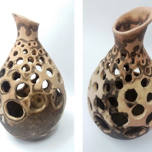 May include: A beige ceramic vase with a distinctive design. The vase has a rounded body with many circular holes and a flared, angled opening. The lower part is a darker brown, contrasting with the lighter upper section. A decorative item.