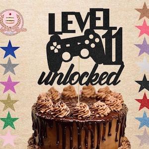 May include: Black glitter cake topper with a video game controller and the text "Level 11 Unlocked".
