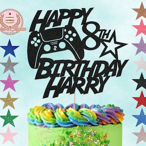 May include: Black glitter cake topper featuring a video game controller, the words "Happy 8th Birthday Harry", and a star. The topper is on a cake with green icing and colourful sprinkles.