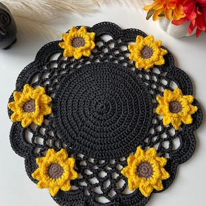 Könnte beinhalten: Schwarze Häkeltischdecke mit gewelltem Rand und sechs gelben gehäkelten Sonnenblumen.