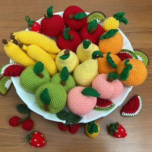 May include: A white bowl filled with crocheted fruit, including apples, pears, bananas, strawberries, oranges, and watermelons. The fruit is arranged in a colorful and appealing display.