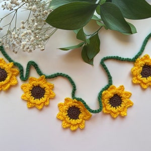 May include: A garland of crocheted sunflowers with green stems. The sunflowers are yellow with brown centers.