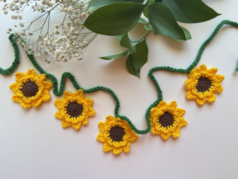 May include: A garland of crocheted sunflowers with green stems. The sunflowers are yellow with brown centers.