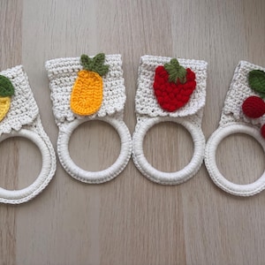 Puede incluir: Cuatro soportes para toallas de ganchillo con anillos blancos y partes superiores cuadradas con apliques de frutas. Los dise&ntilde;os incluyen un lim&oacute;n amarillo con hoja verde, una pi&ntilde;a naranja, una fresa roja y dos cerezas rojas con hojas verdes.