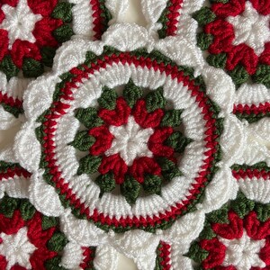 Peut inclure: Gros plan d'une couronne de No&euml;l en crochet avec du fil rouge, blanc et vert. La couronne est compos&eacute;e de plusieurs motifs circulaires avec un motif en &eacute;toile au centre.
