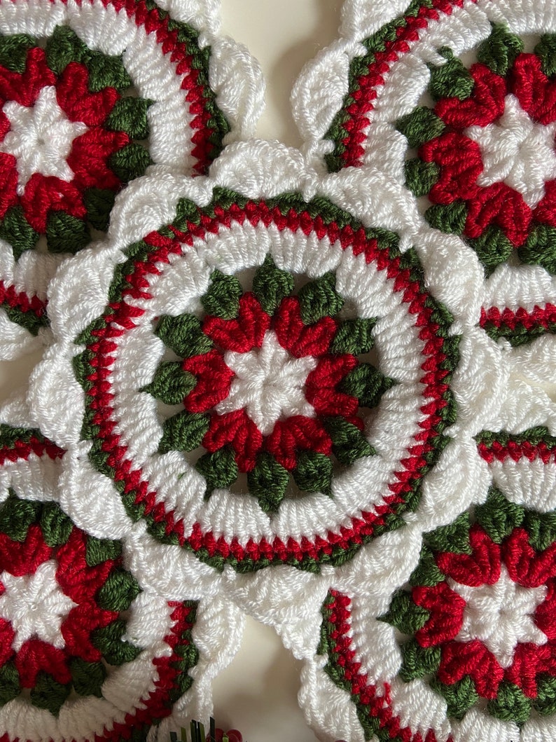 Peut inclure: Gros plan d'une couronne de No&euml;l en crochet avec du fil rouge, blanc et vert. La couronne est compos&eacute;e de plusieurs motifs circulaires avec un motif en &eacute;toile au centre.