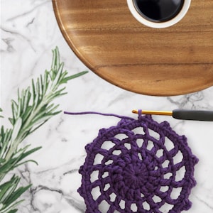 May include: A purple crocheted doily with a spiral design. The doily is on a white marble surface.
