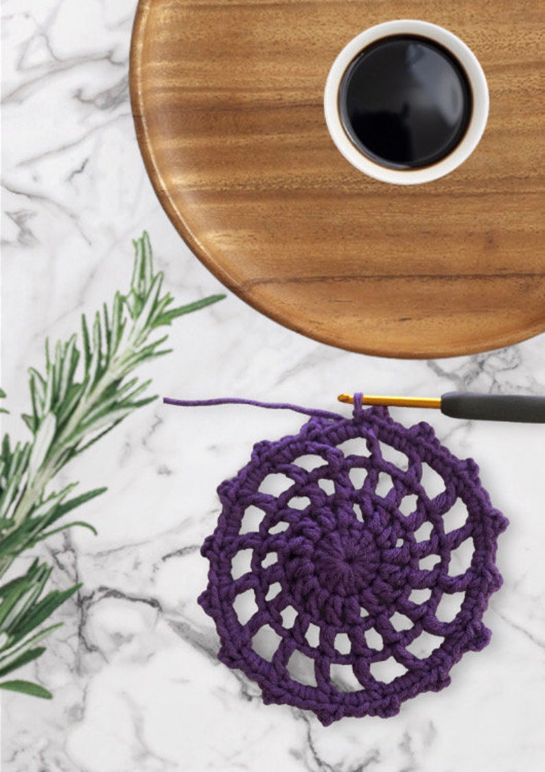 May include: A purple crocheted doily with a spiral design. The doily is on a white marble surface.