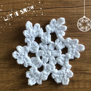 May include: White crocheted snowflake ornament with the text "Let it Snow" in the background.