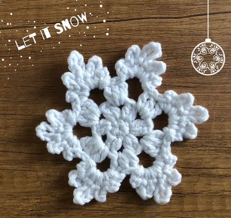 May include: White crocheted snowflake ornament with the text "Let it Snow" in the background.