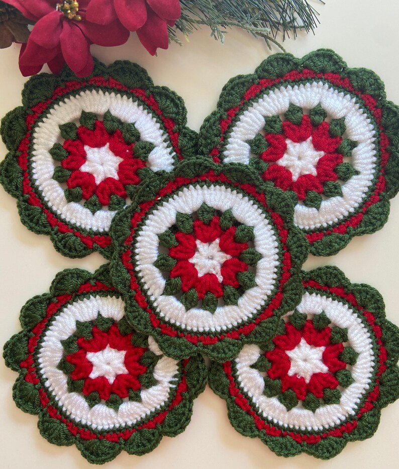 Peut inclure: Ensemble de cinq dessous-de-verre en crochet de couleur verte, blanche et rouge avec un motif de poinsettia.