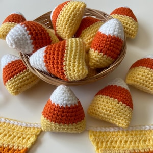 Puede incluir: Una cesta llena de adornos de maíz dulce de crochet en naranja, amarillo y blanco. Los adornos están dispuestos en una cesta con un patrón tejido.