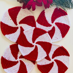 Peut inclure: Quatre dessous-de-verre en crochet rouge et blanc en forme de sucettes de No&euml;l. Les dessous-de-verre sont dispos&eacute;s en cercle, les pointes des sucettes de No&euml;l &eacute;tant tourn&eacute;es vers l'ext&eacute;rieur.