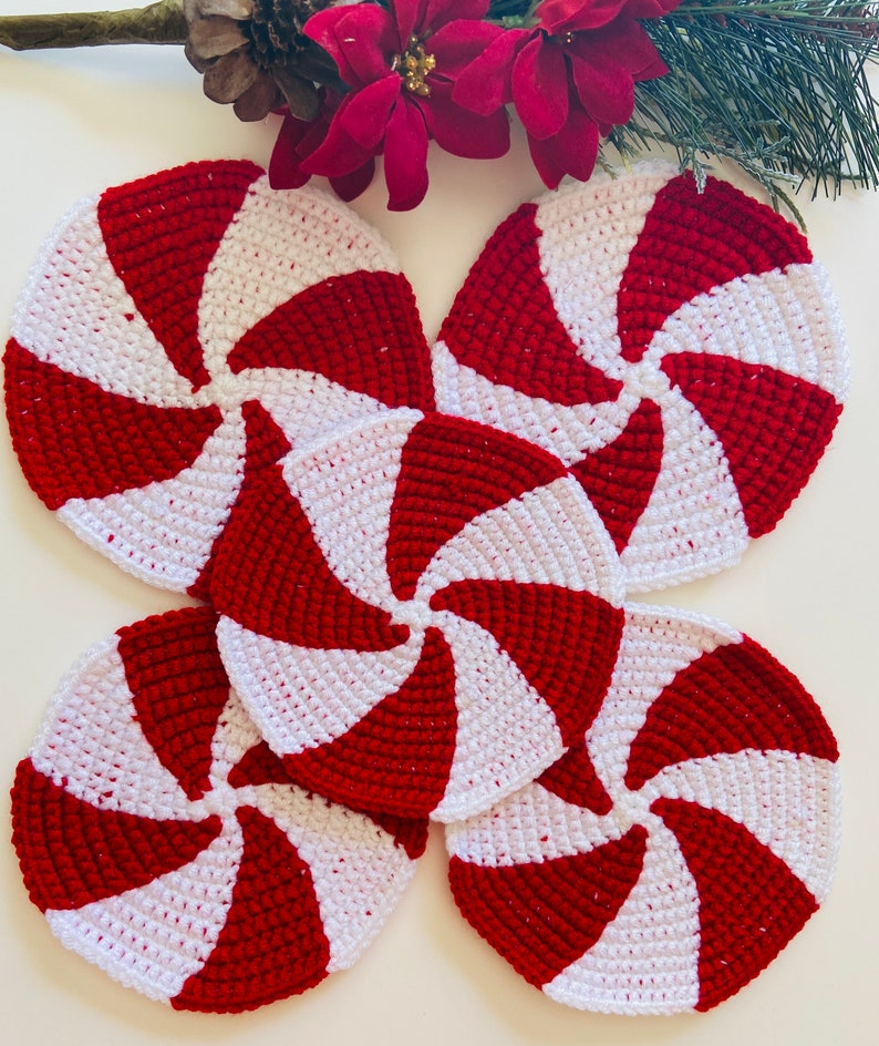 Peut inclure: Quatre dessous-de-verre en crochet rouge et blanc en forme de sucettes de No&euml;l. Les dessous-de-verre sont dispos&eacute;s en cercle, les pointes des sucettes de No&euml;l &eacute;tant tourn&eacute;es vers l'ext&eacute;rieur.