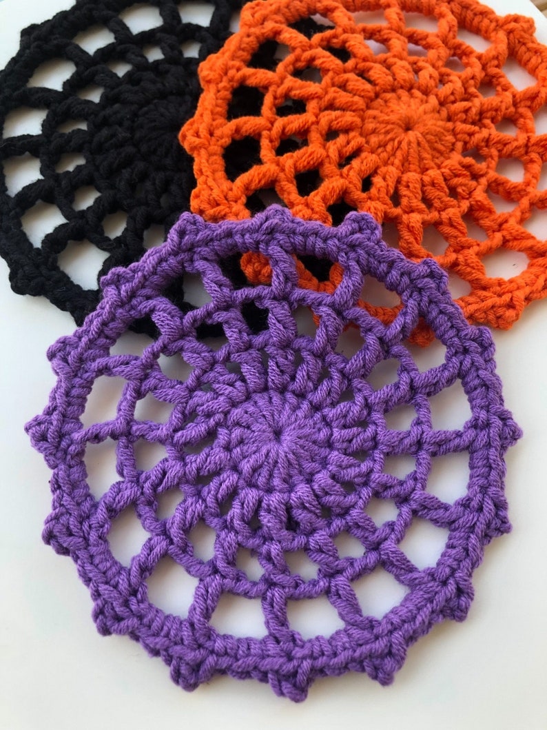 May include: Three crocheted doilies in black, orange, and purple. The doilies have a circular shape with a spiderweb design.