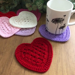 May include: Set of crocheted heart-shaped coasters in pink, white, purple, and red. The coasters are made with a simple stitch pattern and are perfect for adding a touch of handmade charm to your home.