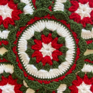 Peut inclure: Gros plan sur quatre dessous-de-verre en crochet rouge, blanc et vert. Chaque dessous-de-verre pr&eacute;sente un motif en forme d'&eacute;toile au centre.