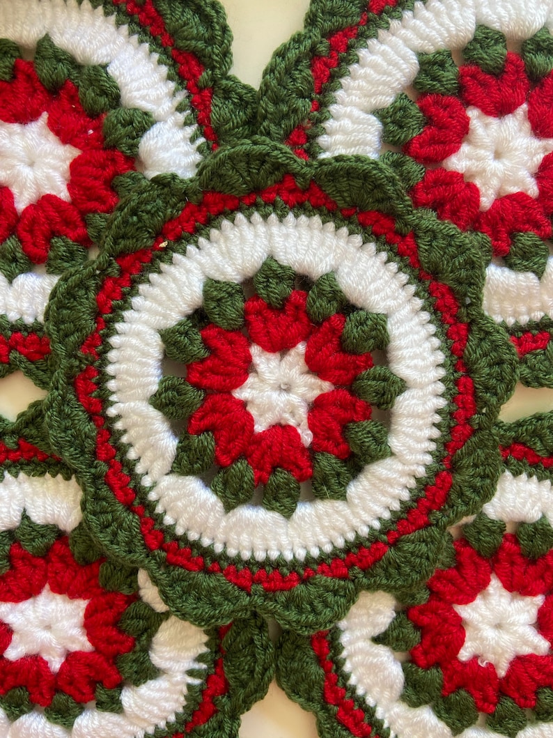 Peut inclure: Gros plan sur quatre dessous-de-verre en crochet rouge, blanc et vert. Chaque dessous-de-verre pr&eacute;sente un motif en forme d'&eacute;toile au centre.