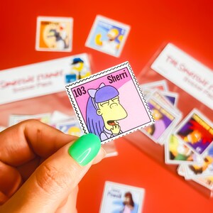 May include: A pink and white cartoon character sticker with the text "Sherri" and "103" on a pink background. The character has purple hair and is wearing a pink dress. The sticker is part of a set of cartoon character stickers.