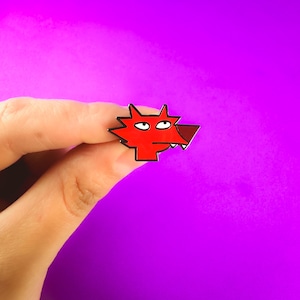 May include: Red enamel pin featuring a cartoon wolf face. The wolf has a black outline and a surprised expression.