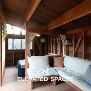 Puede incluir: Interior de una cabaña de madera con suelo y paredes de madera clara. La cabaña cuenta con un sofá empotrado con cojines blancos y cojines decorativos. El texto "ELEVATED SPACES" es visible.