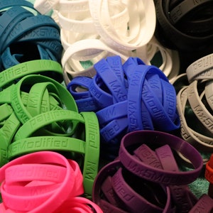 May include: A collection of colourful silicone wristbands with the text "Mx5Modified" printed on them. The wristbands are in various colours, including green, blue, purple, pink, grey, and white.