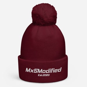 Puede incluir: Gorro de lana burdeos con un pompón blanco y texto blanco bordado que dice "Mx5Modified Est.2020".