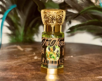 May include: A small hexagonal glass perfume bottle filled with light green liquid, featuring a gold-colored ornate cap and a black label with gold text reading The Master Architect, depicting a figure holding a globe and a cat.