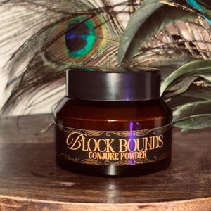 May include: A dark brown jar with a black lid, labeled "Block Bounds Conjure Powder" in gold script. The jar sits on a wooden surface, with peacock feathers and greenery in the background.