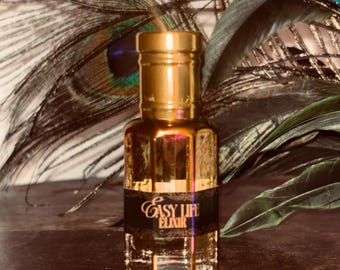 May include: A gold-colored perfume bottle with a black label that reads "Easy Life Elixir." The bottle has a geometric design and a gold cap. The background includes peacock feathers and dark green leaves.