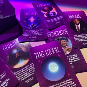 Op de afbeelding: Een set paarse tarotkaarten met illustraties en tekst. De kaarten tonen thema's als geloof, blootstelling, verandering, de maan, oma en oom. De kaarten liggen op een donker oppervlak.