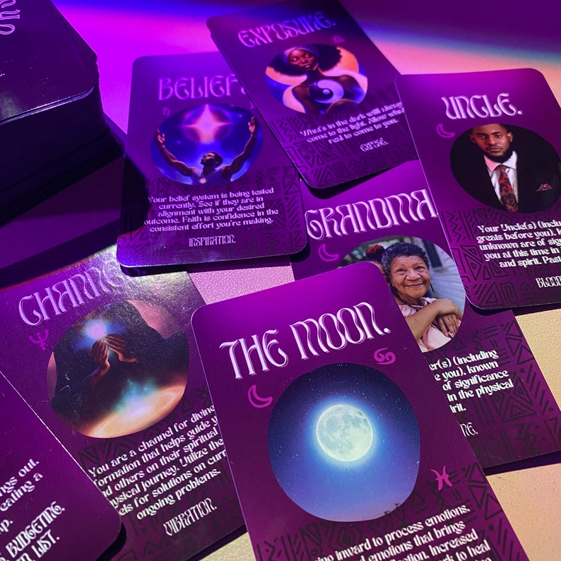 Op de afbeelding: Een set paarse tarotkaarten met illustraties en tekst. De kaarten tonen thema's als geloof, blootstelling, verandering, de maan, oma en oom. De kaarten liggen op een donker oppervlak.