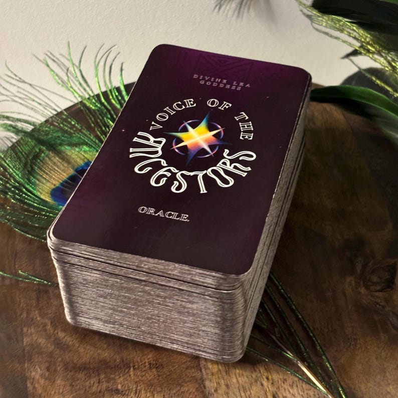 Op de afbeelding: Een deck orakelkaarten met een paarse achtergrond en een gouden sterburst-ontwerp. De tekst op de kaart luidt "Voice of the Ancestors Oracle".