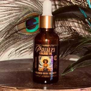 May include: A brown glass bottle with a gold cap and white dropper. The label reads "Psalm 23 Conjure Oil" with an illustration of a person. The bottle is on a wooden surface with peacock feathers in the background.
