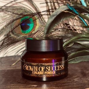 Op de afbeelding: Een klein, bruin glazen potje met een zwart deksel. Op het potje staat in gouden letters "Crown of Success Conjure Powder". De achtergrond toont pauwenveren.