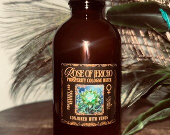 May include: A dark brown glass bottle with a black cap. The label reads "Rose of Jericho Prosperity Cologne Water" with additional text. The label features a floral design and the words "Prosperity and Reviving" and "Conjured with Venus".