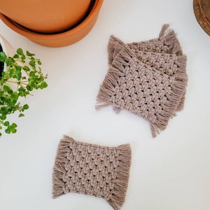 May include: Set of four brown crocheted coasters with fringe detailing. The coasters are made of a soft, natural material and are perfect for protecting surfaces from heat and scratches.