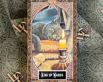 May include: King of Wands tarot card featuring a black cat with green eyes looking at a lit candle in a candlestick. The card has a brown border with gold accents and the text "King of Wands" in a gold font.