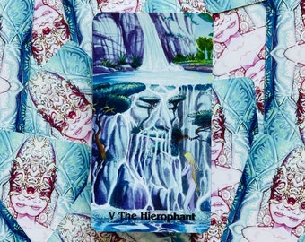 May include: A tarot card with a purple, blue, and green illustration of a waterfall and a woman standing in front of it. The card is titled "V The Hierophant".