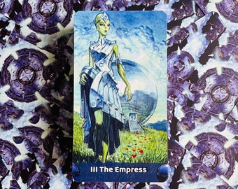 May include: A tarot card with a green-skinned woman in a silver dress standing in a field with a large silver sphere behind her. The card is titled "III The Empress".