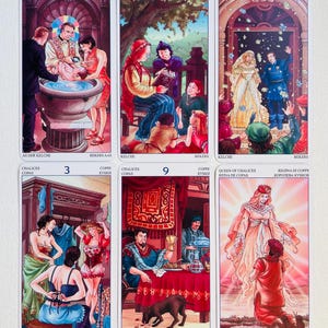May include: Tarot card deck featuring ten cards from the Cups suit. The cards are illustrated with colorful scenes depicting various stages of life, from a baptism to a wedding. The cards are numbered 1 through 10 and include the Ace, Queen, and King of Cups.